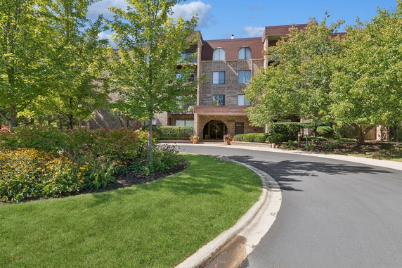 Front view of a multi-story brick building with a driveway and landscaped garden.
