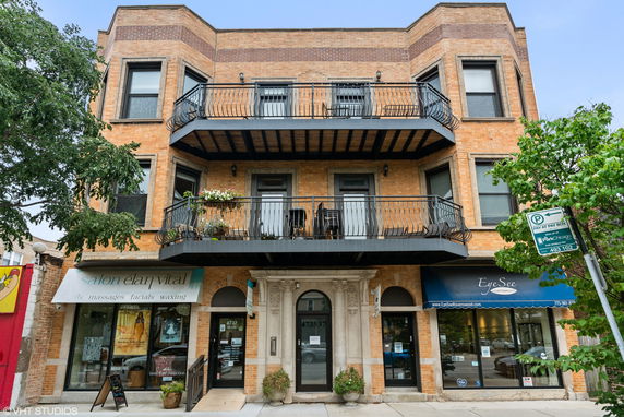 Front view of a three-story brick building with balconies and commercial storefronts on the ground level.