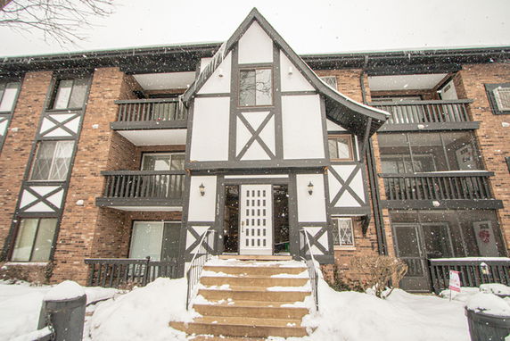 Front view of a multi-story residential building with brick and timber exterior, set in a snowy environment.