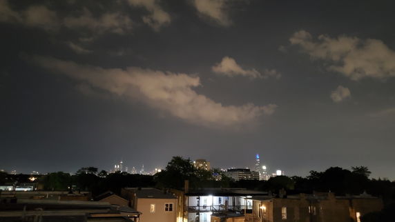 Wide night view of a city skyline with illuminated buildings and cloudy sky.
