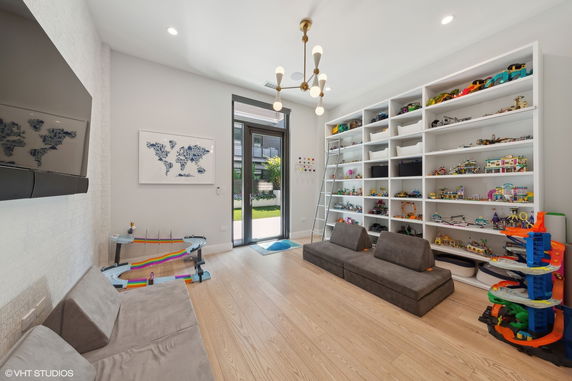 Room with large shelves filled with toys and games, cushioned seats, and a chandelier.