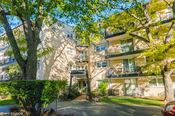 Front view of a multi-story apartment building with balconies and a driveway entrance.