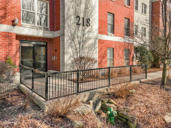 Front view of a multi-story brick building with a black metal railing and entrance door.