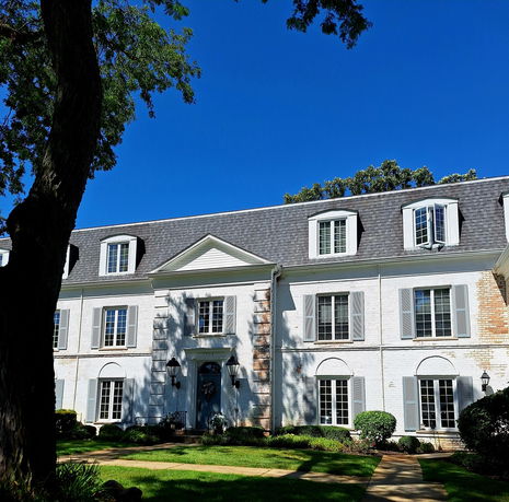 Front view of a large two-story house with dormer windows and a slate roof.