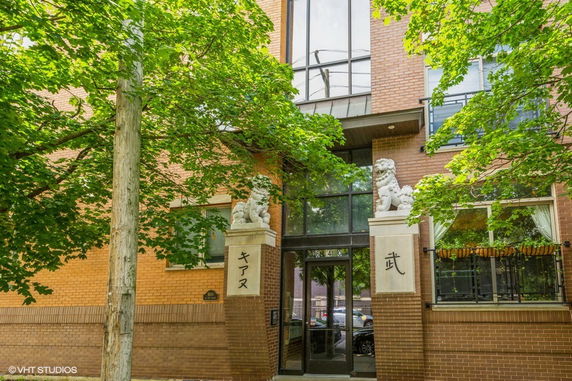 Front view of a brick building with large glass windows and statues at the entrance.