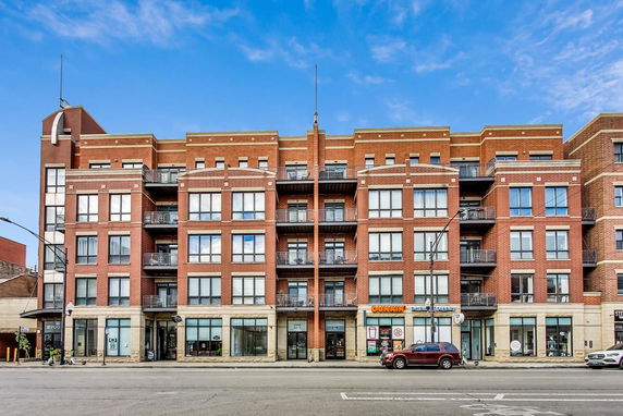 Front view of a multi-story brick building with balconies and street-level shops.