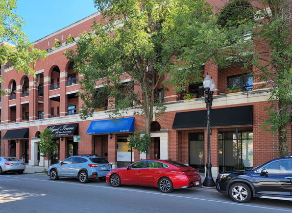 Front view of a multi-story brick building with arches and multiple storefronts.