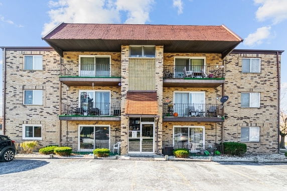 Front view of a three-story apartment building with balconies and brick exterior.