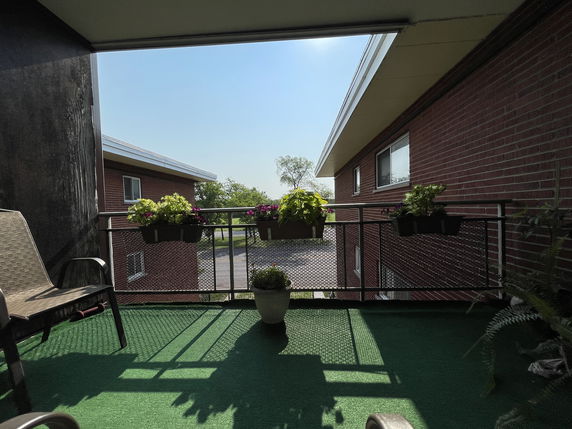 View from a balcony showing parts of a two-story brick building and surrounding trees.