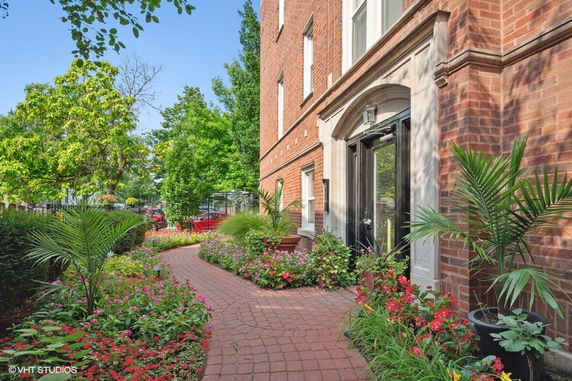 Front view of a brick building with a paved walkway and surrounding garden.