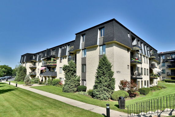 Front view of a multi-story apartment building with balconies and a brick facade.