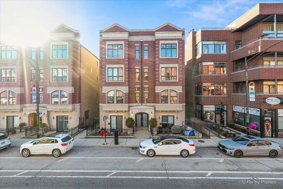 Front view of a four-story red brick building with large windows and a stone base, situated in an urban street setting.