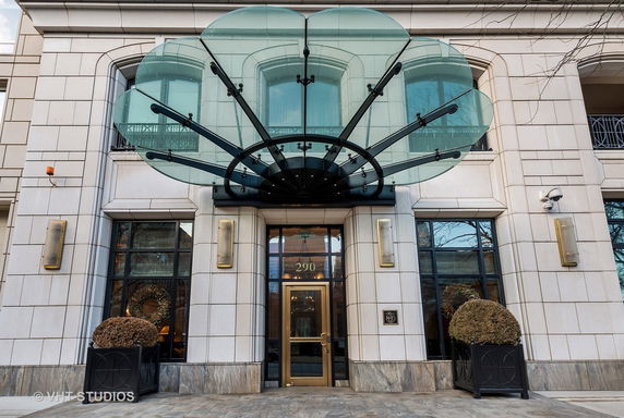 Front view of a building with a glass canopy and stone facade.