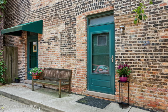 Front view of a brick building with green doors and a bench.