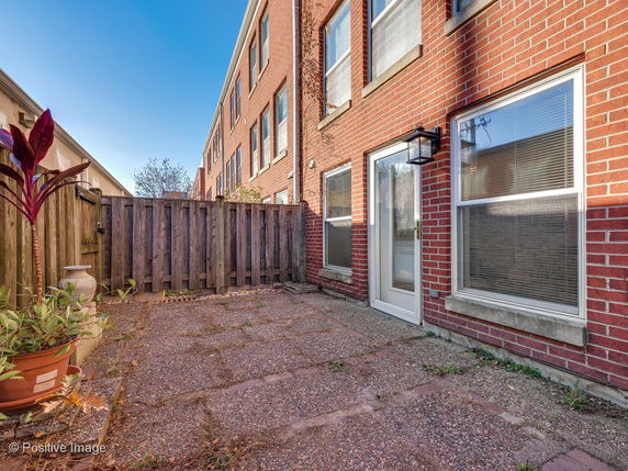 Back view of a multi-story brick townhouse with a small paved yard.