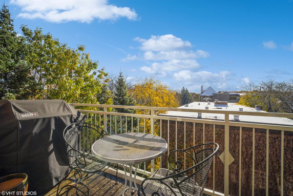 Balcony view overlooking treetops and rooftops with outdoor seating and a grill.