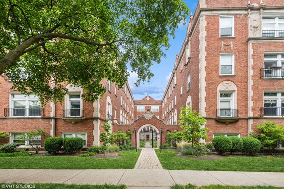 Front view of a brick apartment building with decorative arch and manicured landscaping.