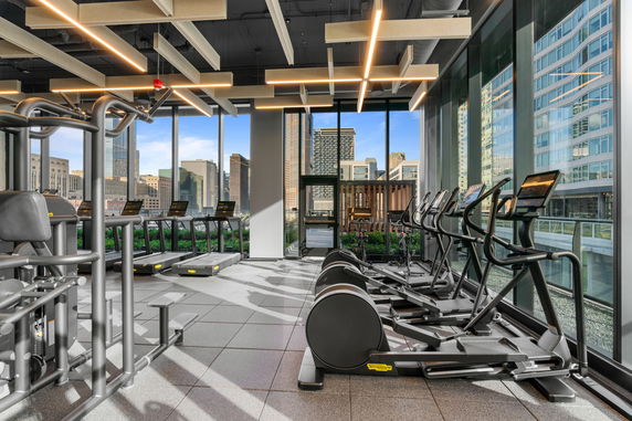 Gym area with exercise machines and city view through large windows.