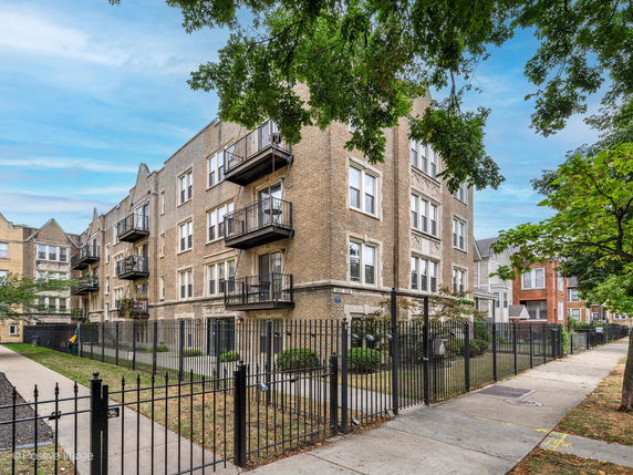 Front view of a multi-story apartment building with balconies and a fenced front yard.
