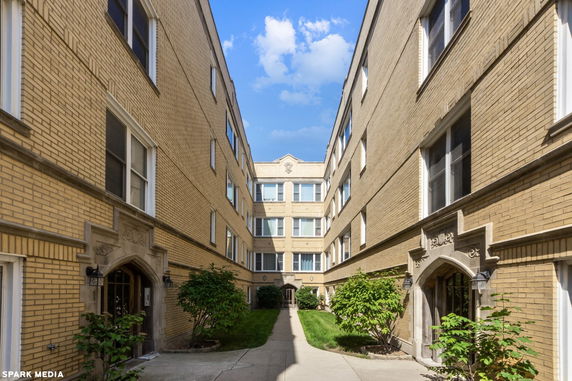Front view of a multi-story brick apartment building with an entrance path.