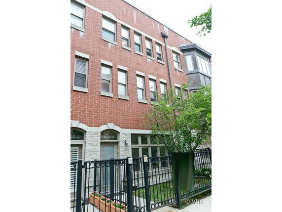 Front view of a multi-story brick building with multiple windows and an entrance gate.
