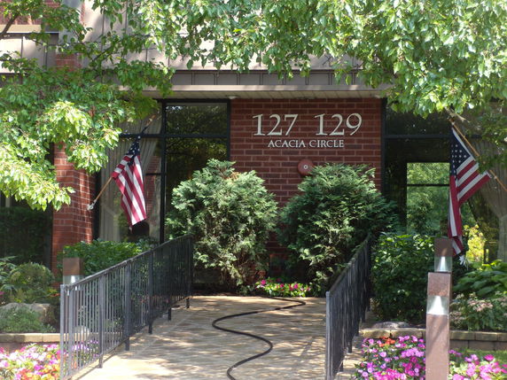 Front view of a building with a ramp leading to the entrance, flanked by potted plants and American flags.