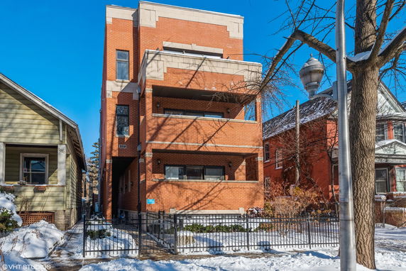 Front view of a multi-story brick building with balconies and a gated entrance.
