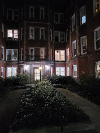 Front view of a multi-story brick building at night with numerous windows and a central entrance.