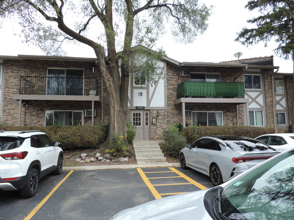 Front view of a multi-story apartment building with balconies and parked cars in front.