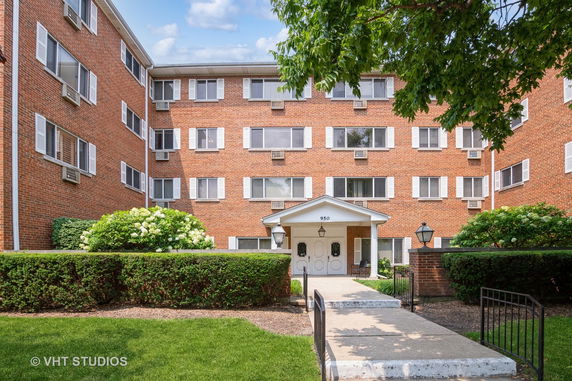 Front view of a multi-story brick apartment building with white window shutters and a covered entrance.