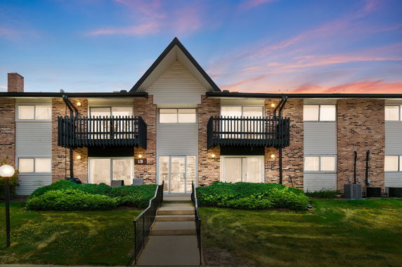 Front view of a two-story residential building with balconies and a sloped roof.