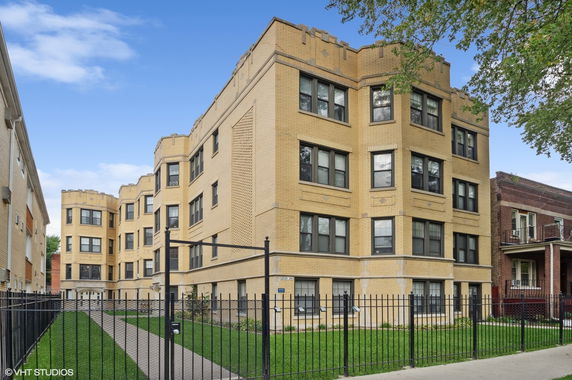 Front view of a multi-story brick apartment building with fenced entry.
