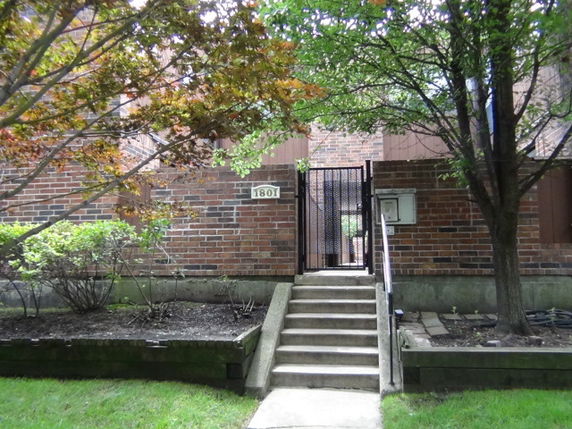 Front view of a brick house with steps leading to a gated entrance.