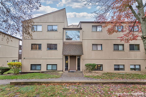 Front view of a multi-story apartment building with beige siding and various windows.