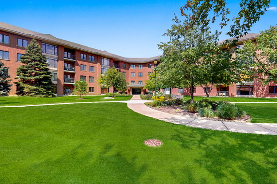 Front view of a multi-story brick apartment building with green lawn and pathways.
