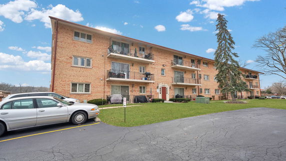 Front view of a three-story brick apartment building with balconies.