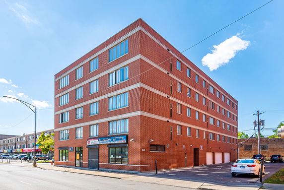 Front view of a multi-story brick building with multiple windows and a parking area on the side.
