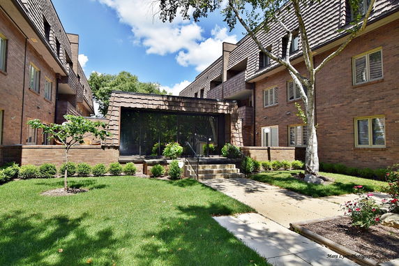 Front view of a multi-story brick building with landscaped entrance and large windows.