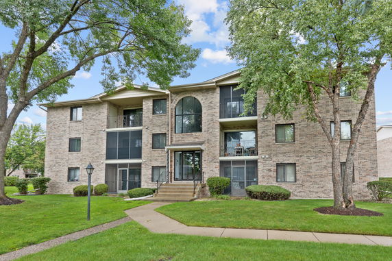 Front view of a three-story brick apartment building with balconies and large windows.