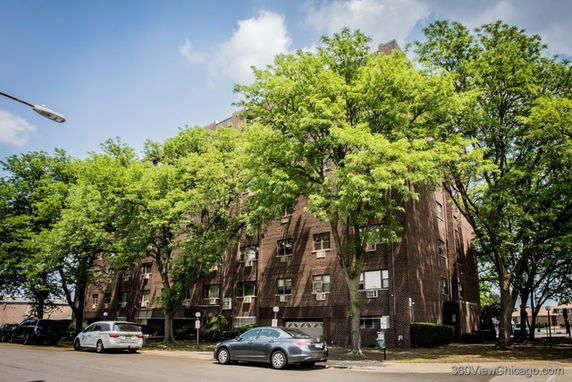 Front view of a multi-story brick apartment building with several windows and cars parked in front.