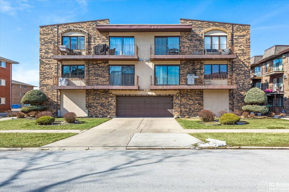 Front view of a three-story brick apartment building with balconies and a central garage.