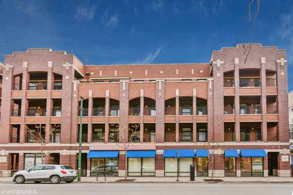 Front view of a multi-story brick building with balconies and storefronts on the ground level.