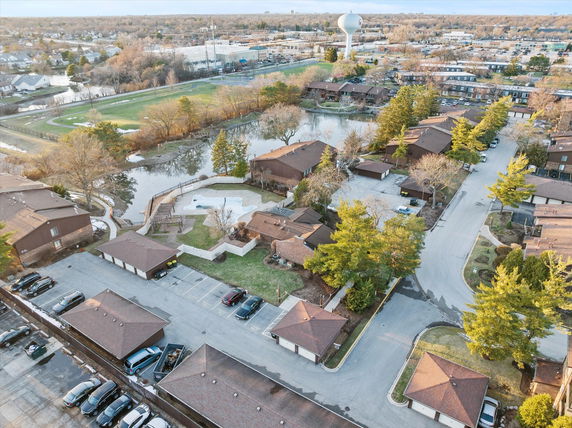 Aerial panoramic view of a residential area with multiple houses, a pond, parking spaces, and a water tower in the background.