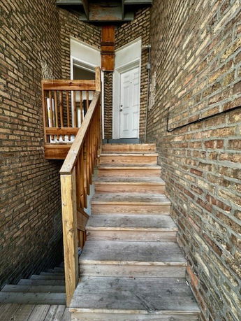 View of an external staircase leading up to a door in a brick building.