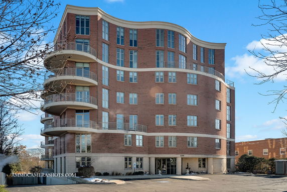 Front view of a multi-story brick building with curved balconies and large windows.
