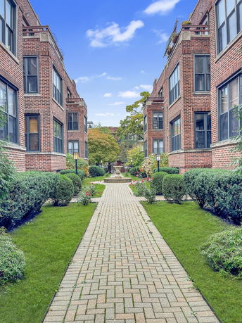 Elevated view of a brick apartment complex with symmetrical buildings on either side of a landscaped walkway.