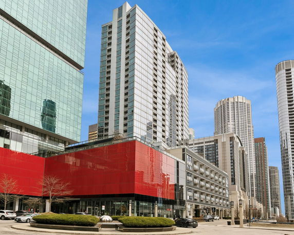 Front view of a modern skyscraper with glass facade and red accent building in an urban setting.