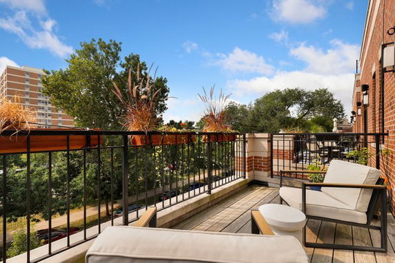 Outdoor balcony with seating overlooking trees and a building in the background.