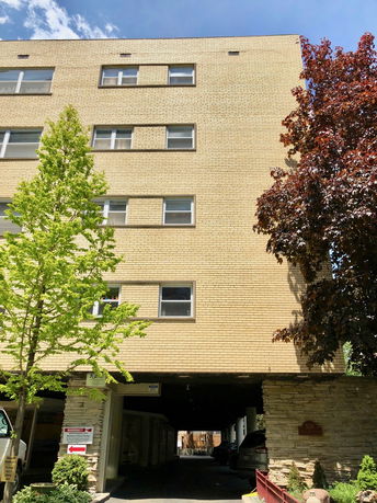 Front view of a multi-story brick building with parking space under the structure.
