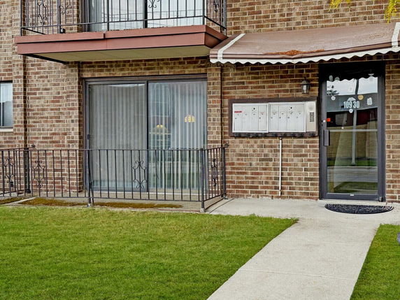 Front view of a brick building with a balcony and entrance with mailboxes.